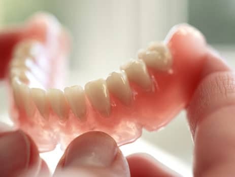 Close-up of a denture with soft liner material showing tooth-colored crowns and pink gum base.