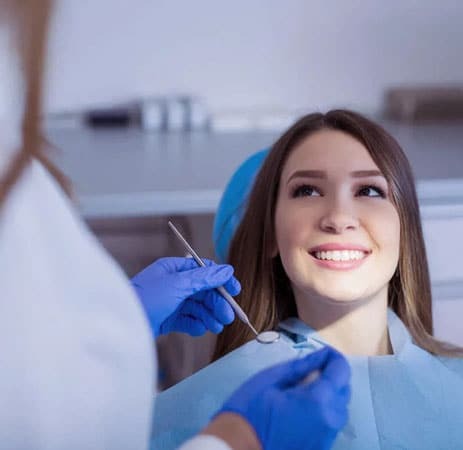 Smiling female patient in dental bib with dentist holding mirror during examination.
