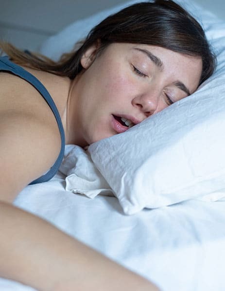 Woman sleeping peacefully on white bedding, illustrating restful sleep after sleep apnea treatment.