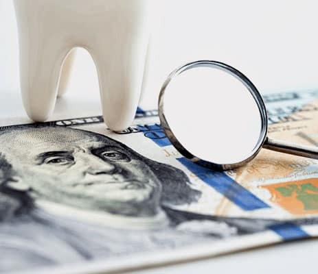 Dental insurance concept showing magnifying glass over US dollar bill and tooth model.