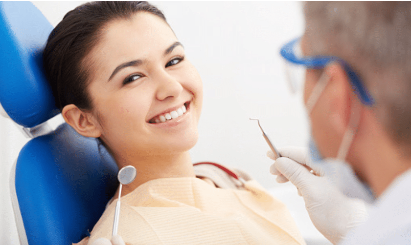 Woman smiling in dental chair during consultation with dentist holding tools.