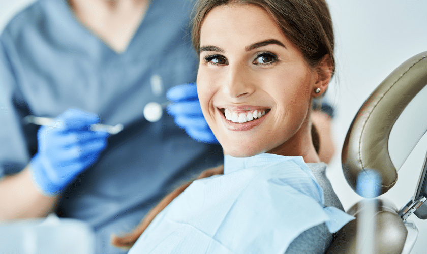 Woman smiling in dental chair while dentist examines her teeth during soft liner denture consultation.