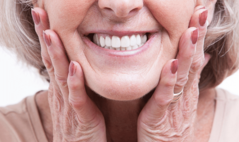 Mature woman smiling with hands framing her face, displaying healthy white teeth.
