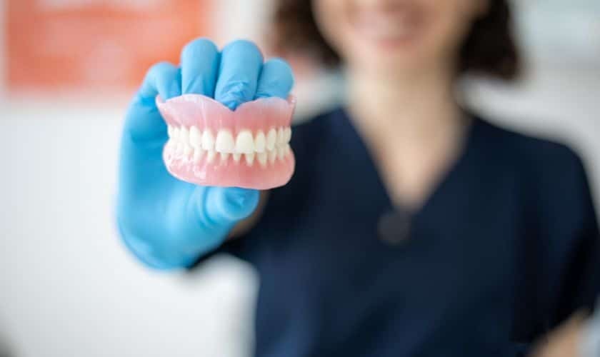 Dental professional holding a denture model showing upper and lower teeth alignment.