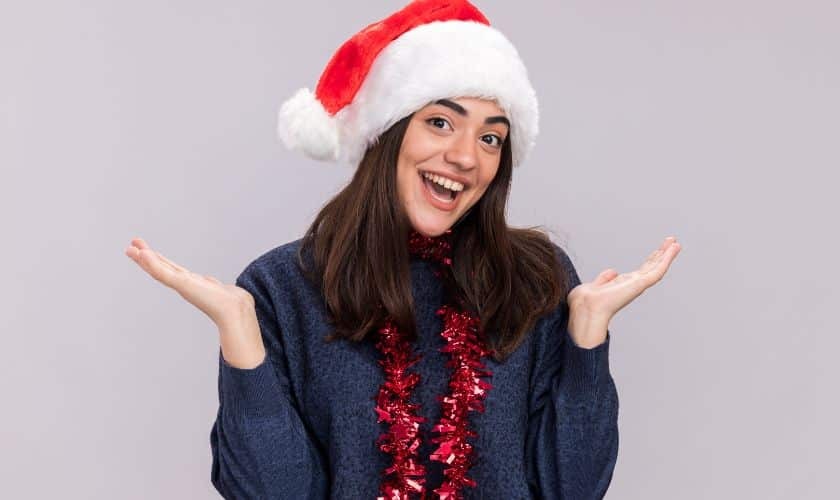 Happy woman in Santa hat and festive attire smiling brightly for holiday dental care.