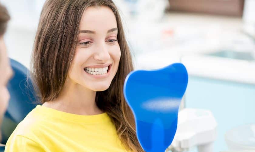 Young woman in yellow shirt smiling in dental office treatment room.