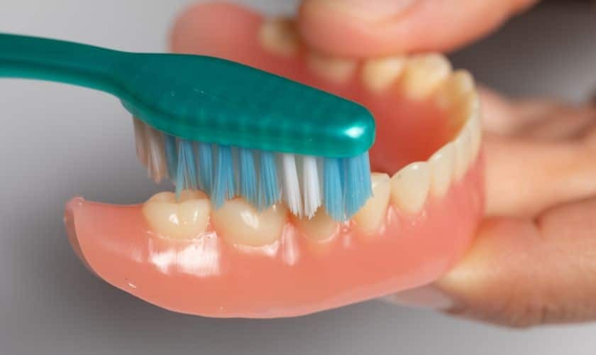 Person brushing dentures with a toothbrush to maintain proper denture hygiene and oral health.