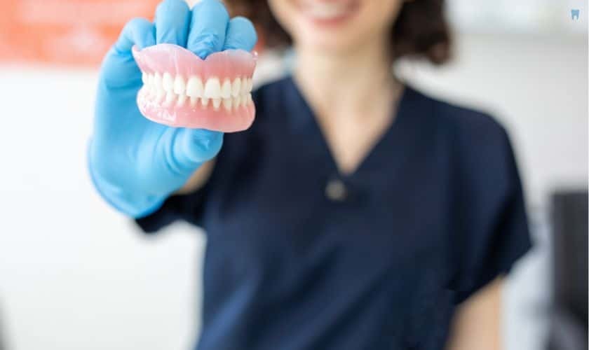 Dental professional holding a model of complete dentures showing teeth alignment and fit.