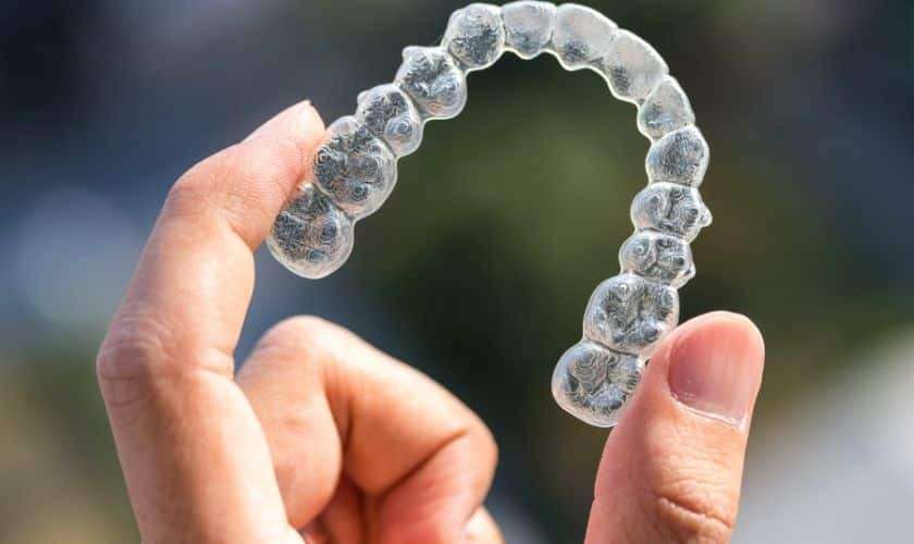 Clear Invisalign aligner tray held between fingers showing transparent dental straightening treatment.