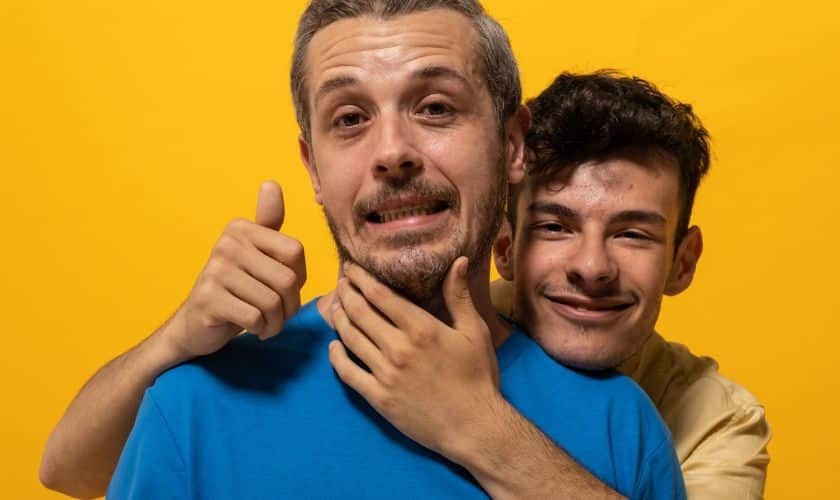 Father and son smiling together against yellow background for Father's Day dental health article.