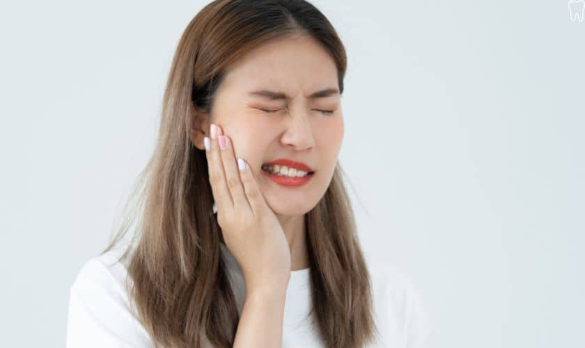 Woman holding her cheek in pain, grimacing with eyes closed, displaying tooth pain symptoms.
