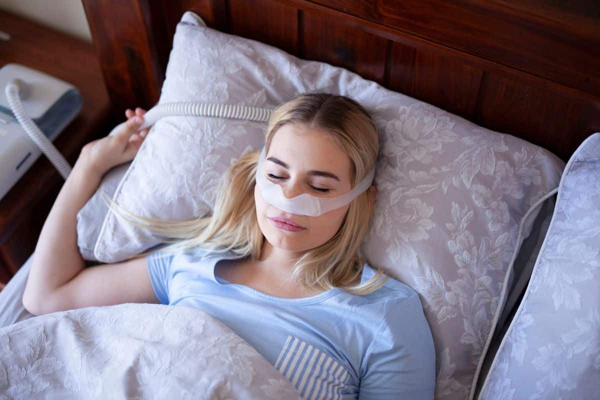 Woman sleeping peacefully wearing a white nose strip for sleep apnea treatment.