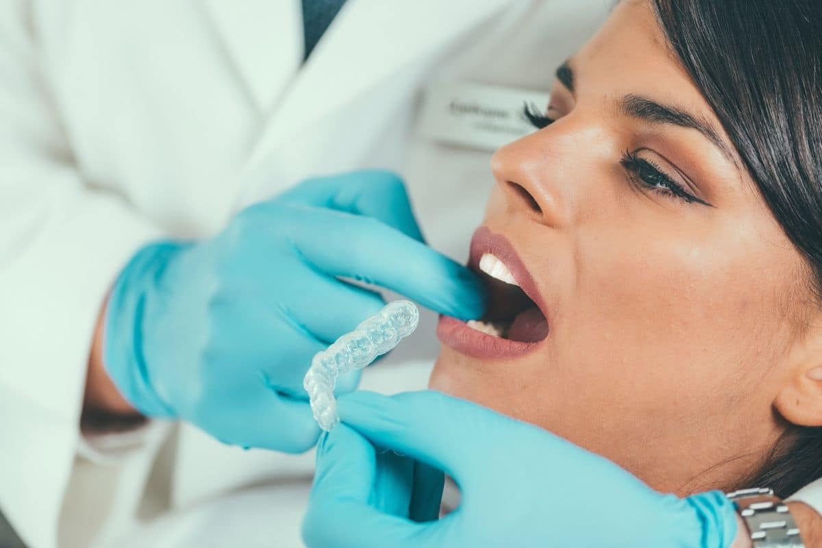 Dentist fitting clear aligner tray into patient's mouth during Invisalign treatment.