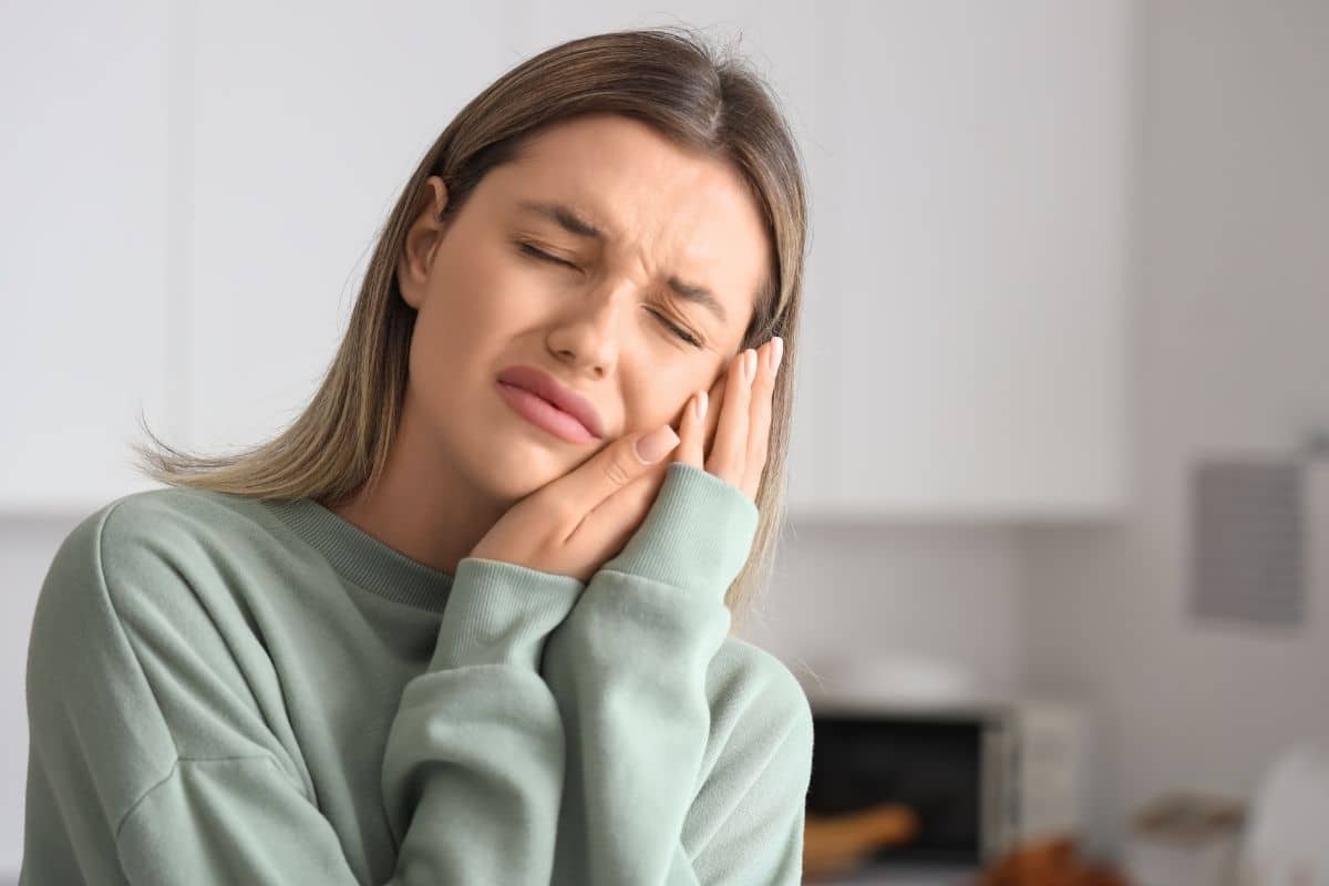 Woman with tooth pain holding her cheek, experiencing winter dental discomfort.
