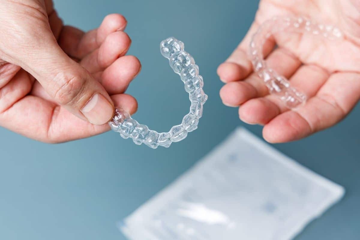 Hands holding a clear Invisalign tray against a blue background.