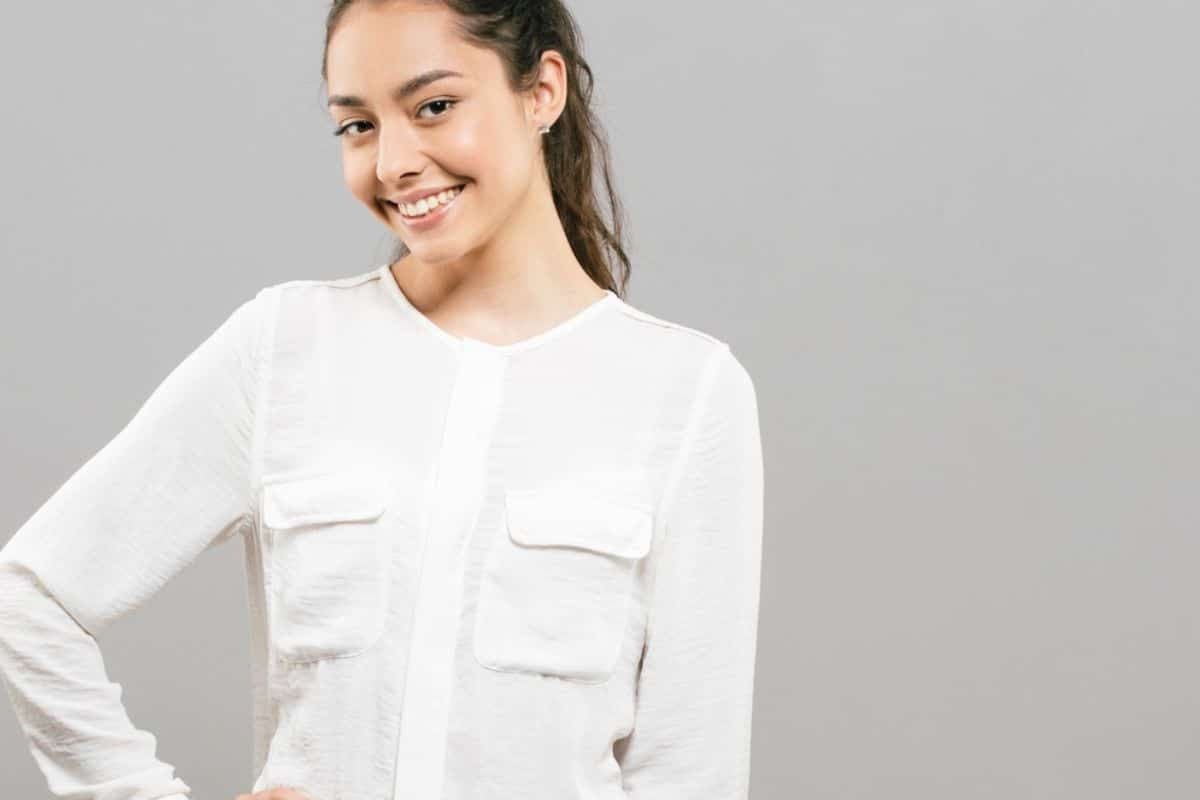 Smiling woman in white clinical shirt representing positive mental health and dental wellness connection.