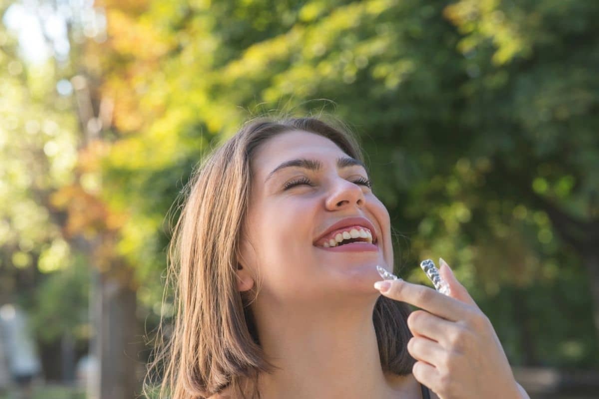 Woman smiling with eyes closed outdoors, displaying results of Invisalign teeth straightening treatment.