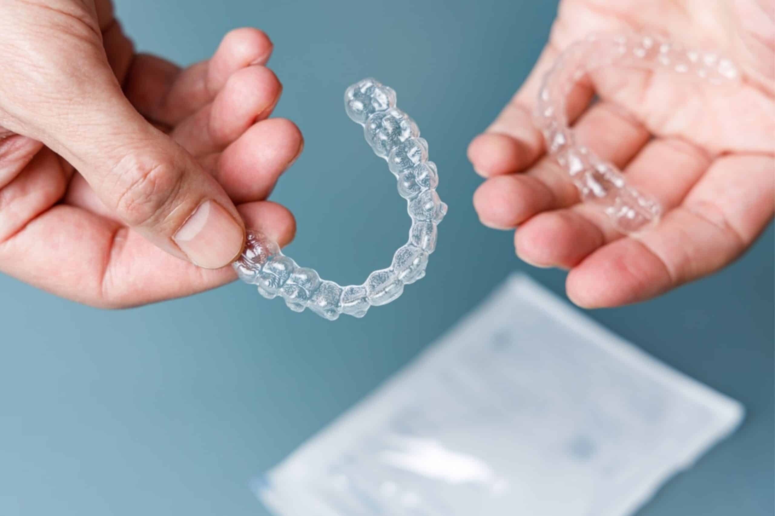 Hands holding a clear Invisalign aligner tray showing teeth straightening treatment.
