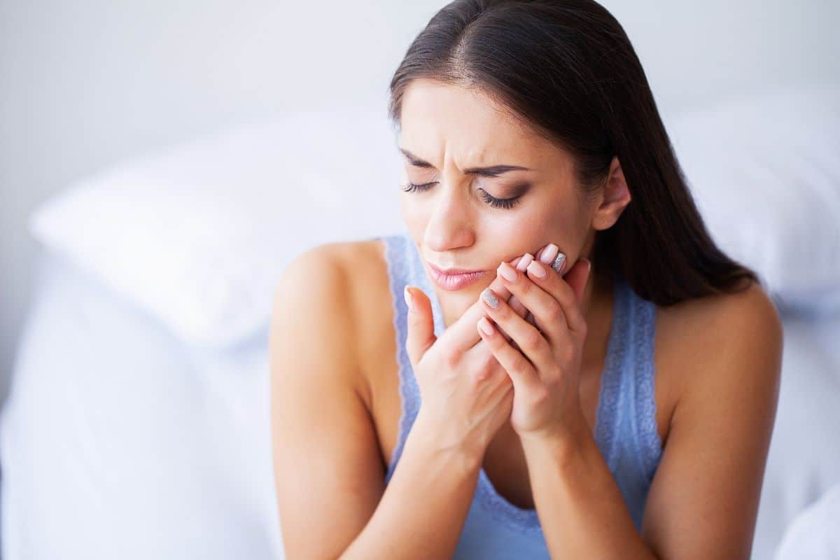 Woman holding her cheek in pain from gum soreness, illustrating common denture discomfort.