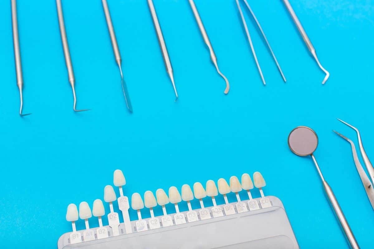 Dental implant shade guide with various tooth color samples and clinical instruments on blue background.