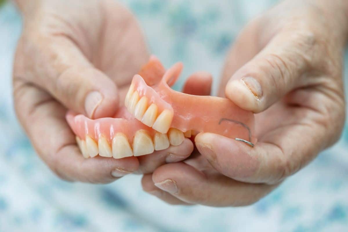 Hands holding a full denture showing tooth discomfort and potential sore areas.
