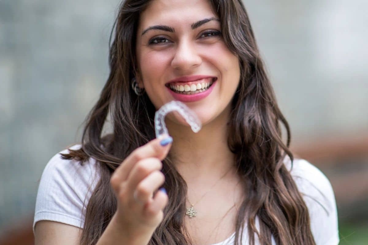 Smiling woman holding clear Invisalign aligner tray for open bite correction treatment.