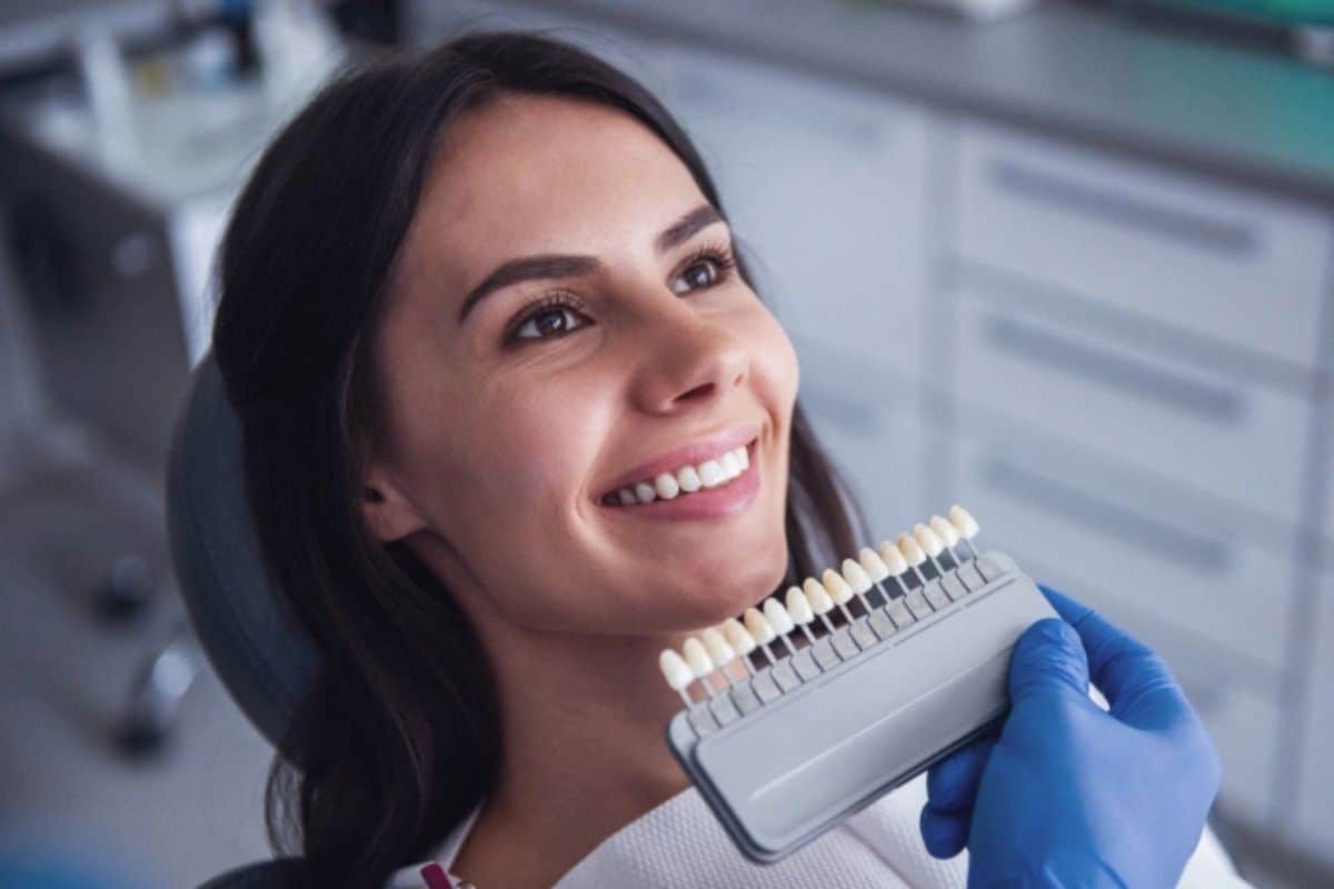 Woman smiling while holding a dental shade guide showing tooth color options for veneers.