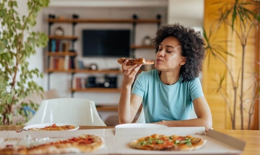 Woman eating pizza at home, experiencing metallic taste after dental implant treatment.