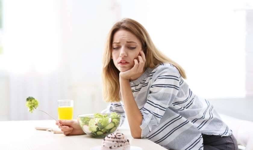 Woman contemplating healthy eating choices with salad and juice, representing preventive nutrition for dental health.