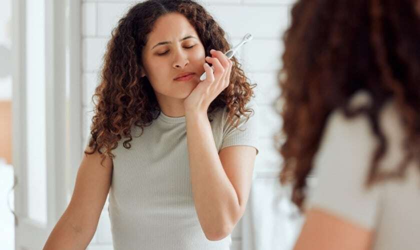 Woman touching her cheek in pain, experiencing tooth discomfort and swollen gums.